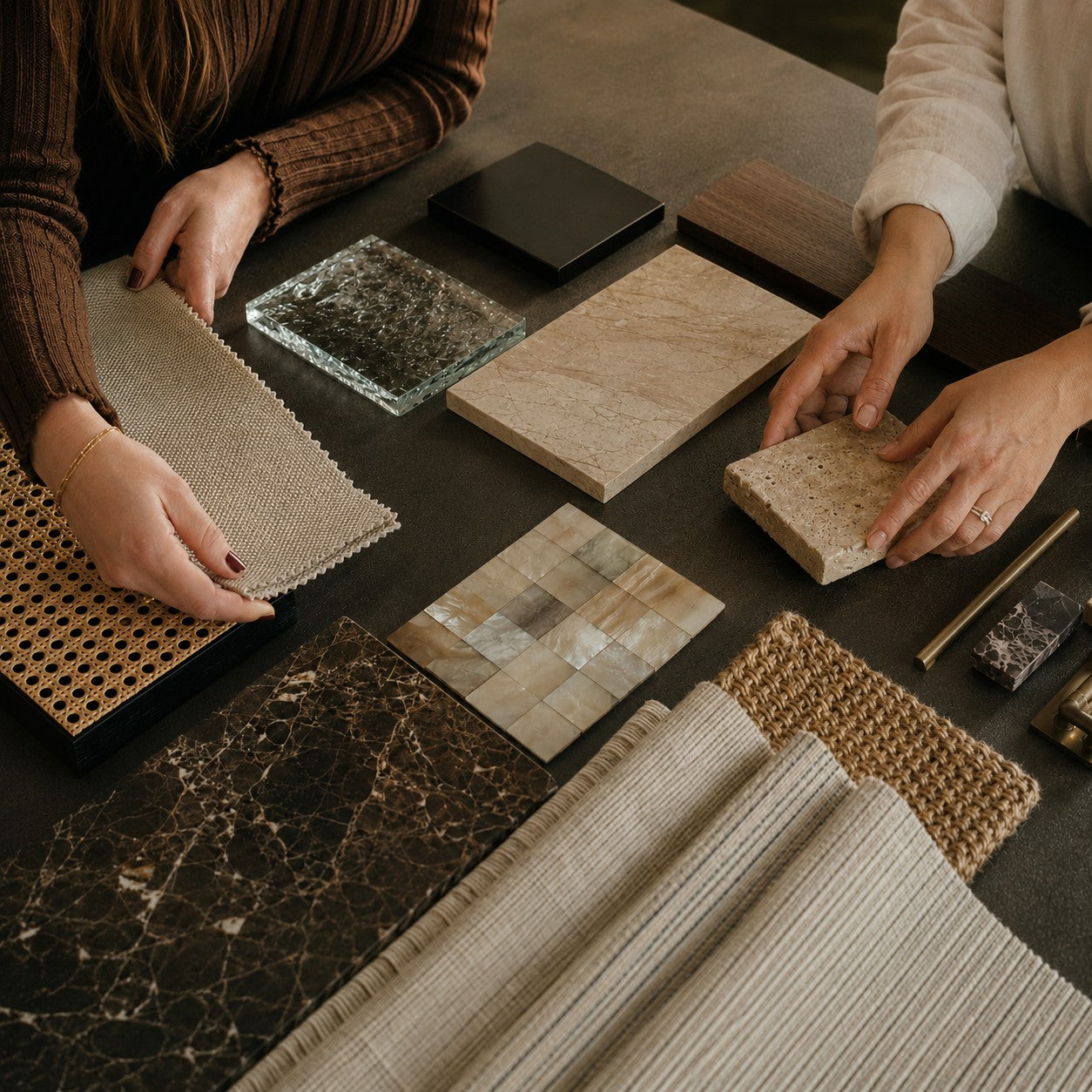 Hands comparing stone, glass, fabric, wood, shell and woven material samples