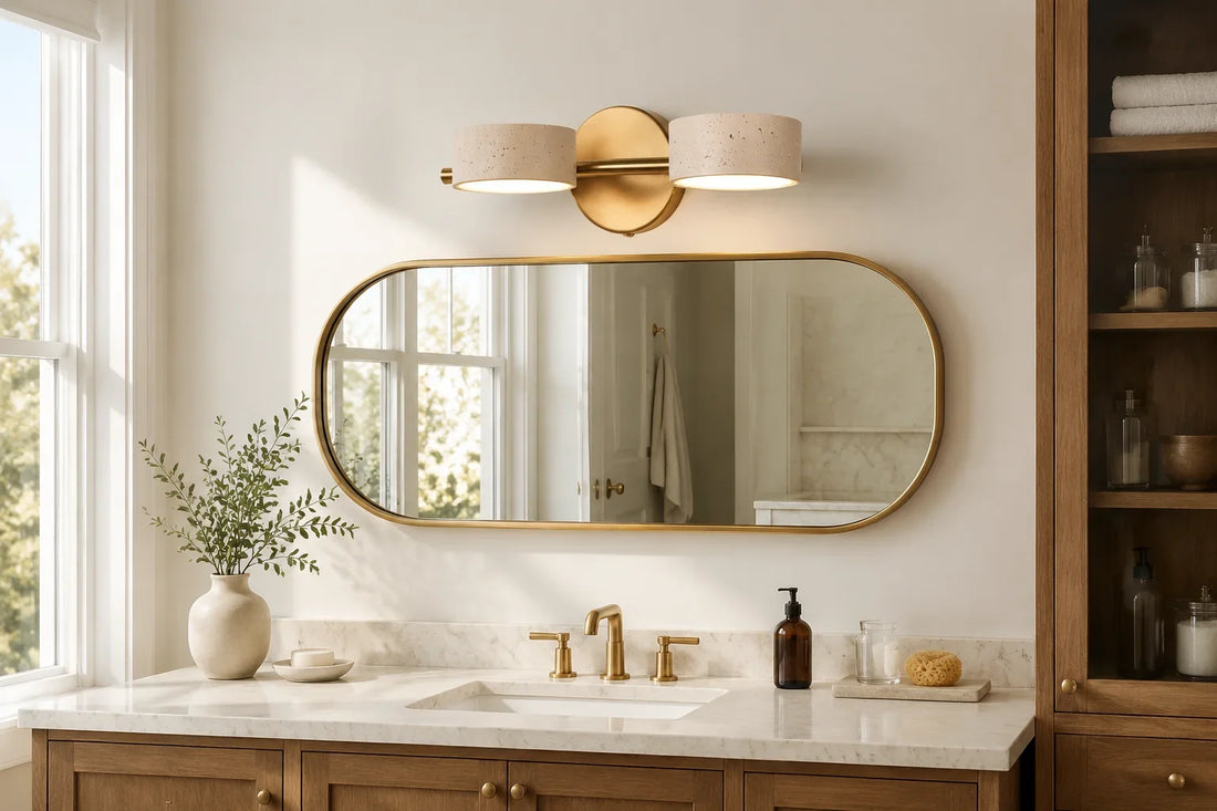 Two-light travertine vanity fixture above a brass bathroom mirror
